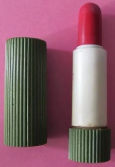 a red and white lipstick sitting on top of a green container next to a pink wall