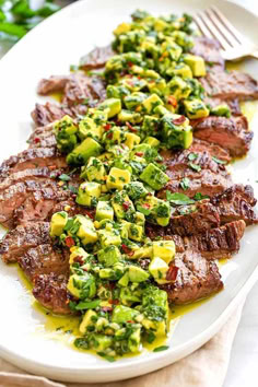 a white plate topped with steak covered in broccoli and cucumber salad