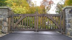 an open wooden gate with stone walls and trees in the background