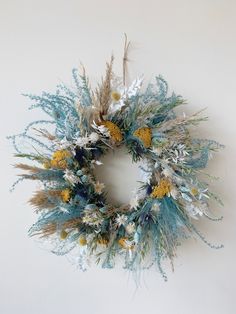 a dried wreath with blue and yellow flowers hanging on the wall in front of a white wall