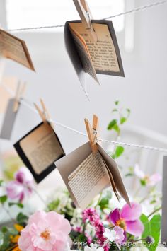 several pieces of paper hanging from a clothes line with flowers in the foreground and notes attached to them