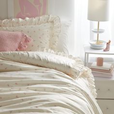 a white bed with pink pillows and blankets on top of it next to a night stand