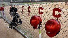 helmets are hanging on the fence at a baseball field