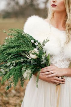 a woman in a white dress holding a bouquet of flowers and greenery with her hand on her hip