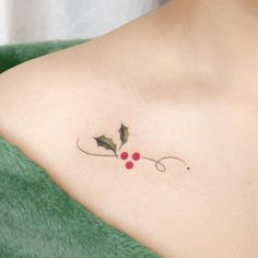 a woman's chest with a small holly tattoo on her left shoulder and red berries on the right side