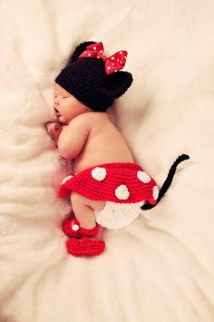 a baby sleeping on top of a bed wearing a minnie mouse hat and diaper