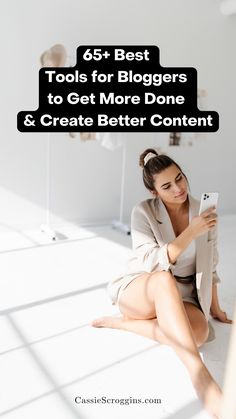 a woman sitting on the floor looking at her cell phone with text overlay that reads 65 best tools for bloggers to get more done & create better content