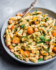 a bowl filled with pasta and vegetables on top of a gray table next to a spoon