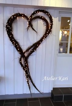 a heart made out of branches with lights on the side of a building in front of a door