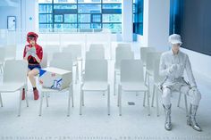 two people sitting on white chairs in an empty room