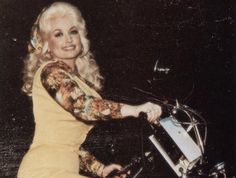 a woman sitting on top of a motorcycle wearing a dress and holding onto the handle bars