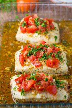 three pieces of fish with tomatoes and parsley on top in a glass baking dish