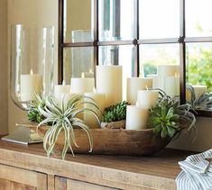 candles and succulents sit in a wooden bowl on a table next to a mirror