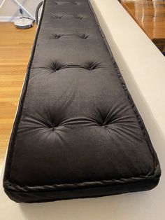 a long black bench cushion sitting on top of a white counter next to a wooden floor