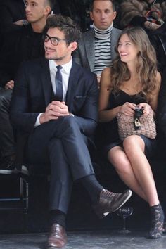 a man and woman sitting next to each other at a fashion show in front of a crowd