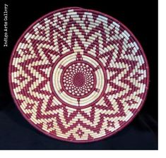 a red and white basket with an intricate design on it's side, sitting on a black surface