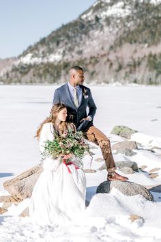 a bride and groom sitting on rocks in the snow