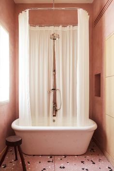 an old fashioned bathtub in a bathroom with pink walls and white curtains on the shower