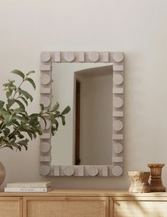 a mirror sitting on top of a wooden dresser next to a potted green plant