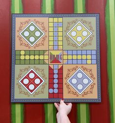 a person holding up a board game on a striped wall with green and red stripes