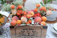 a wooden box filled with peaches and flowers on top of a white table cloth