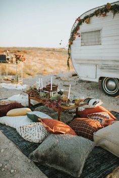 a camper trailer is parked in the desert with pillows and candles on it's table