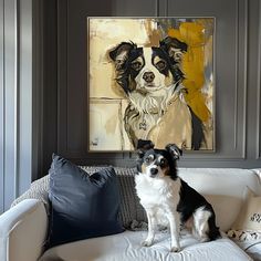 a black and white dog sitting on top of a couch in front of a painting