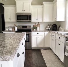 a kitchen with white cabinets and granite counter tops, stainless steel appliances and wood flooring