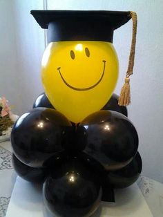 a graduation cap on top of balloons with a smiley face drawn on it's head