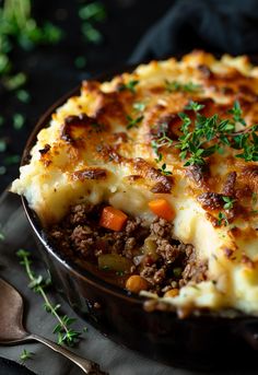 a casserole dish with meat and vegetables in it on a table next to a spoon