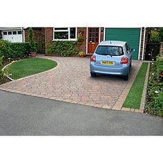 a blue car parked in front of a house with grass and flowers on the driveway