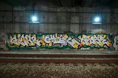 graffiti on the side of a train track in an empty tunnel with lights above it