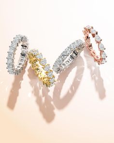 three different colored gold and silver rings with diamonds in them on a pink background,