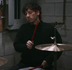 a man sitting in front of a drum set with his hands on the drumstick