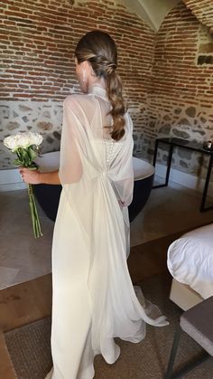 a woman in a white dress holding a bouquet of flowers next to a brick wall