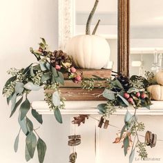 a mantel topped with white pumpkins and greenery on top of a mantle