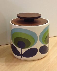 a ceramic container with a wooden lid sitting on top of a wood floor next to a wall