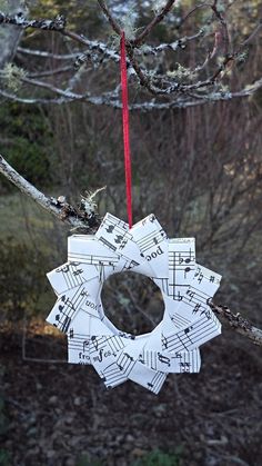 an ornament made out of sheet music is hanging on a tree branch in the woods