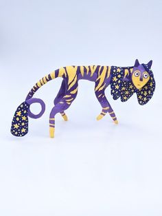 a purple and yellow tiger figurine with scissors in it's paws on a white surface