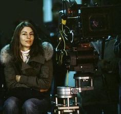 a woman sitting next to a camera in front of other people