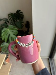 a person holding a pink coffee mug with eyeballs on it and beaded bracelets