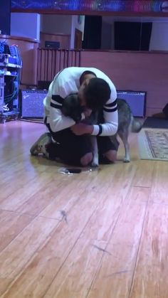 a man kneeling down holding a dog on top of a hard wood floor