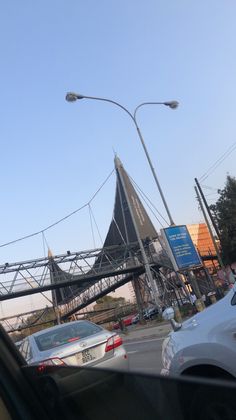 some cars are driving down the street and there is a large triangular structure in the background