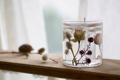 a glass filled with water and flowers on top of a wooden shelf next to a window