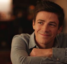 a close up of a person wearing a gray shirt and smiling at the camera with his arms crossed