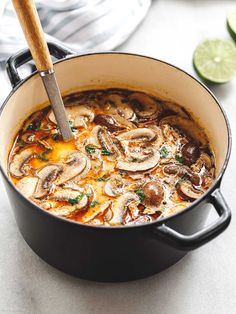 a pan filled with mushrooms and sauce on top of a counter next to sliced limes