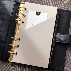 a black and gold planner sitting on top of a bed next to a book bag