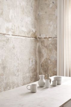 three white vases sitting on top of a table in front of a stone wall