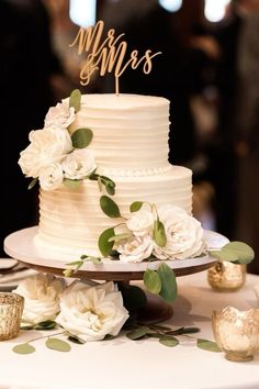 a wedding cake with white flowers and mr and mrs topper sitting on a table