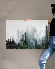 a woman holding up a large painting with trees on the side and fog in the air